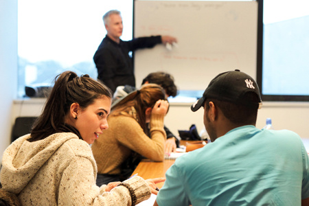 Two young students discussing at the back of a classroom. 