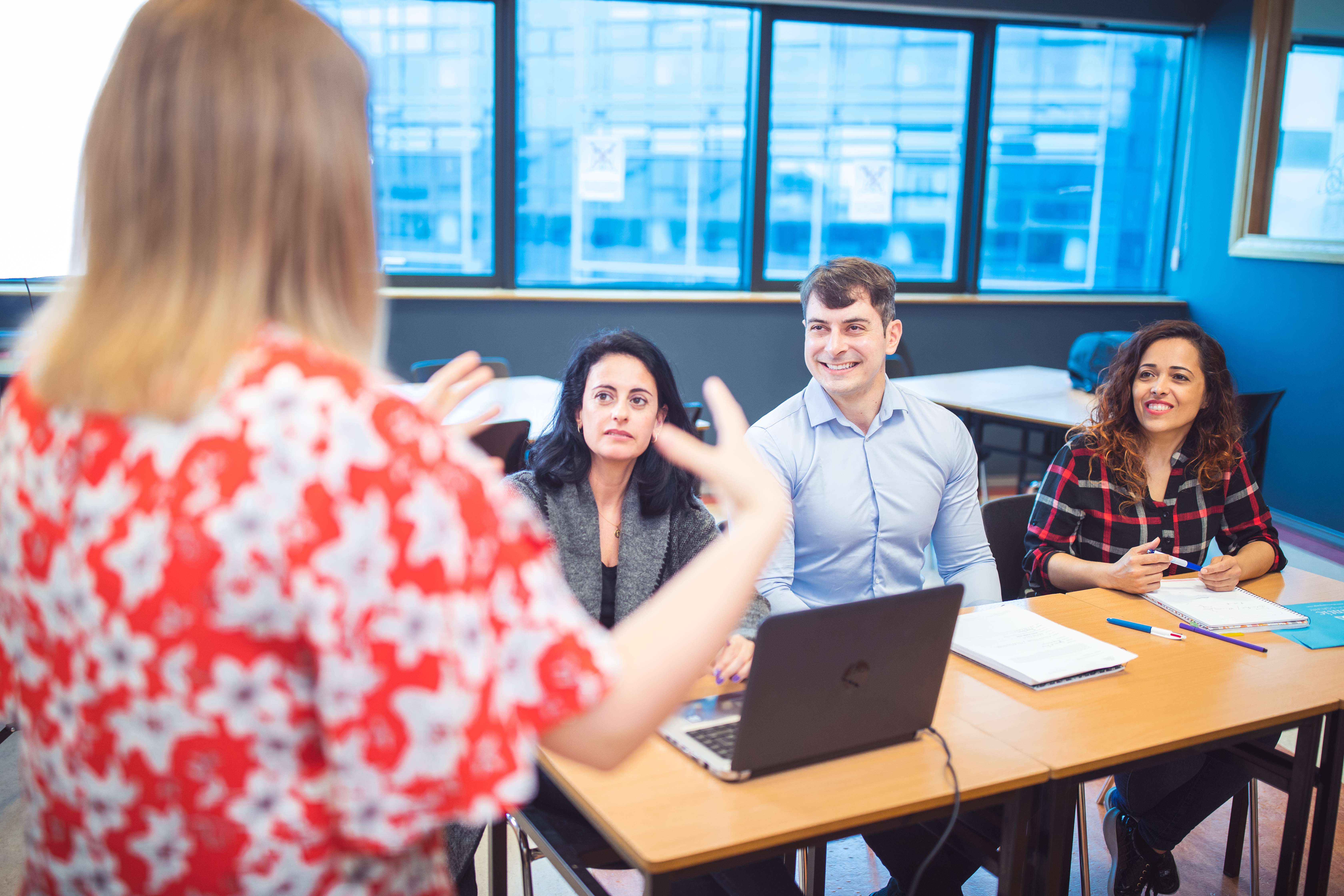 Teacher gesturing to three students sitting in a classroom.