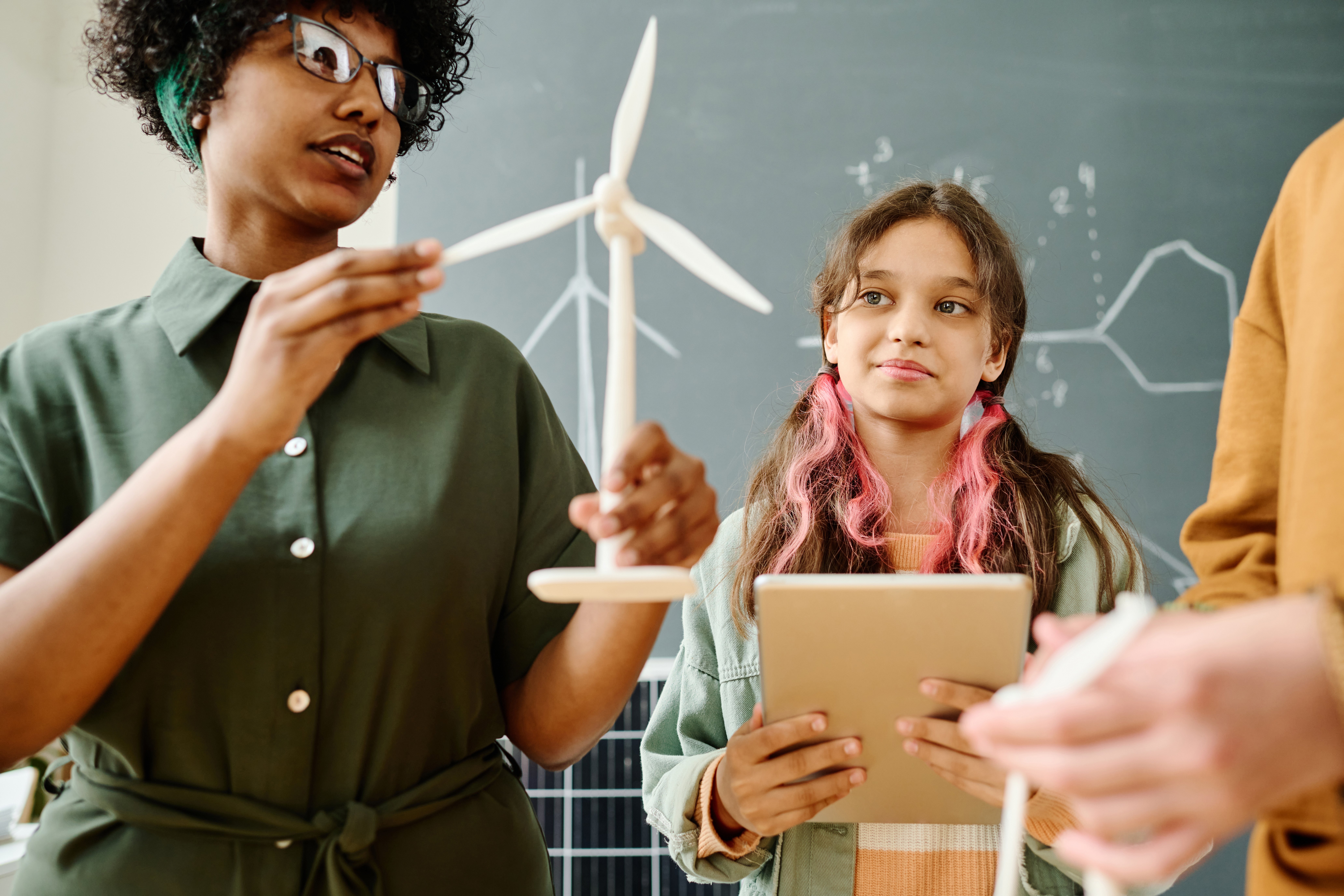 Young female teacher showing a wind turbine to a student while he takes notes.